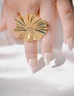 Gold ring with sunburst design on a hand against a white background